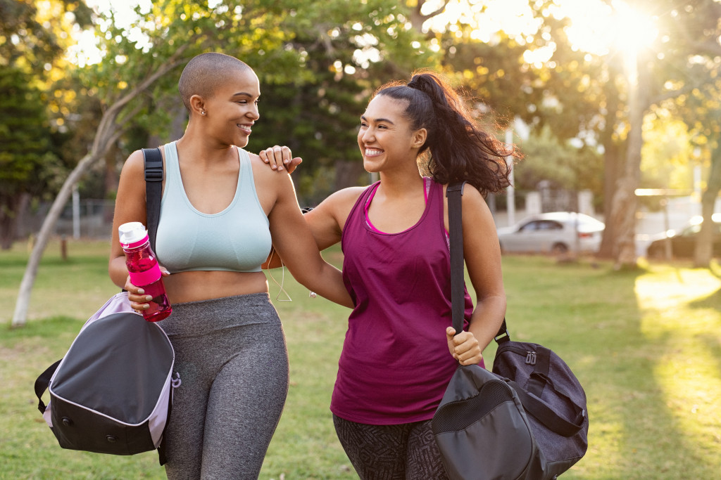 two woman smiling outdoors while carrying gym bags